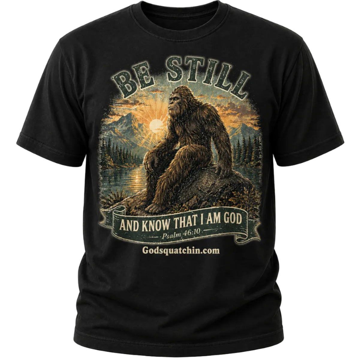 Black t-shirt featuring a vintage-style graphic of Bigfoot sitting calmly on a rock beside a mountain lake at sunrise, surrounded by pine trees and mountains, with the text “Be Still and Know That I Am God – Psalm 46:10”