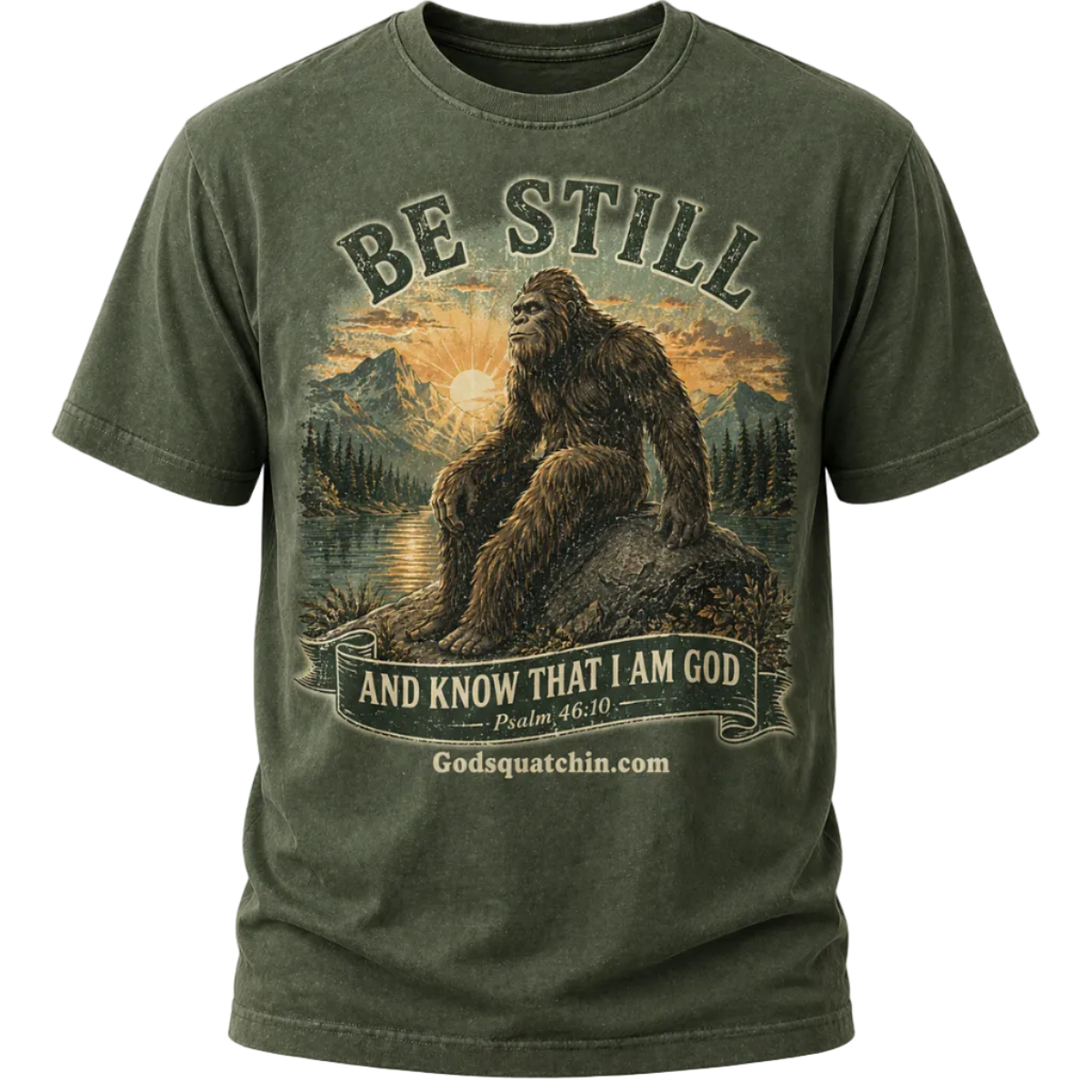 Forest Green t-shirt featuring a vintage-style graphic of Bigfoot sitting calmly on a rock beside a mountain lake at sunrise, surrounded by pine trees and mountains, with the text “Be Still and Know That I Am God – Psalm 46:10”
