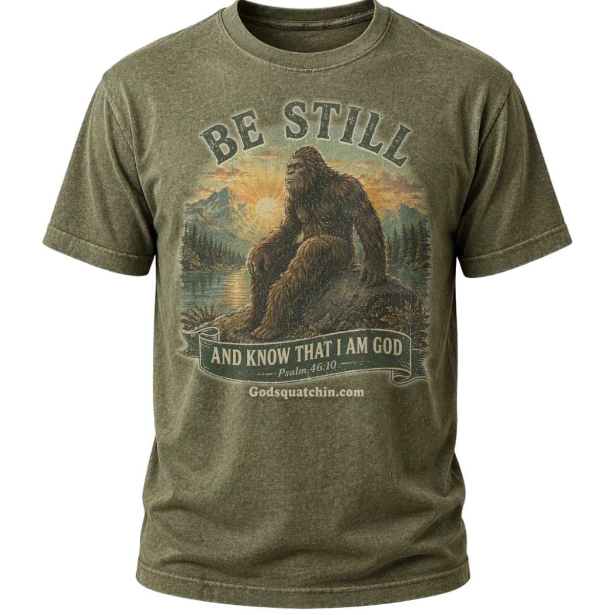 Olive Green t-shirt featuring a vintage-style graphic of Bigfoot sitting calmly on a rock beside a mountain lake at sunrise, surrounded by pine trees and mountains, with the text “Be Still and Know That I Am God – Psalm 46:10”